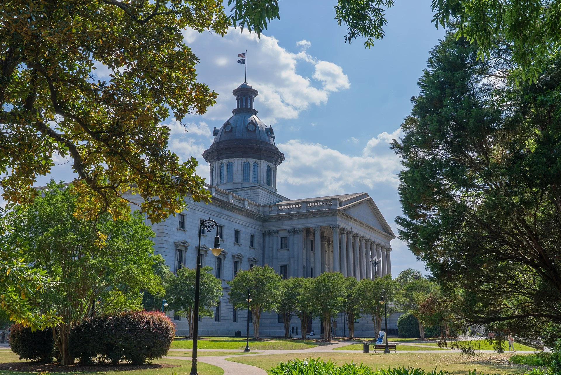 South Carolina State House seen through trees in a sunny garden with a clear blue sky and scattered clouds