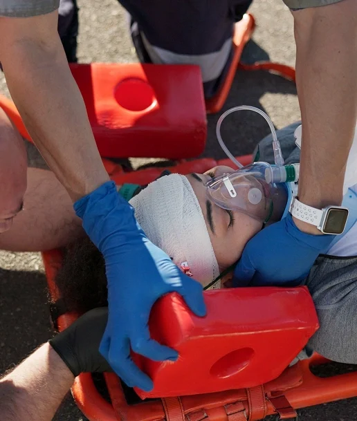 Person with head injury on stretcher receives medical care with oxygen mask and head immobilizer by responders wearing blue gloves