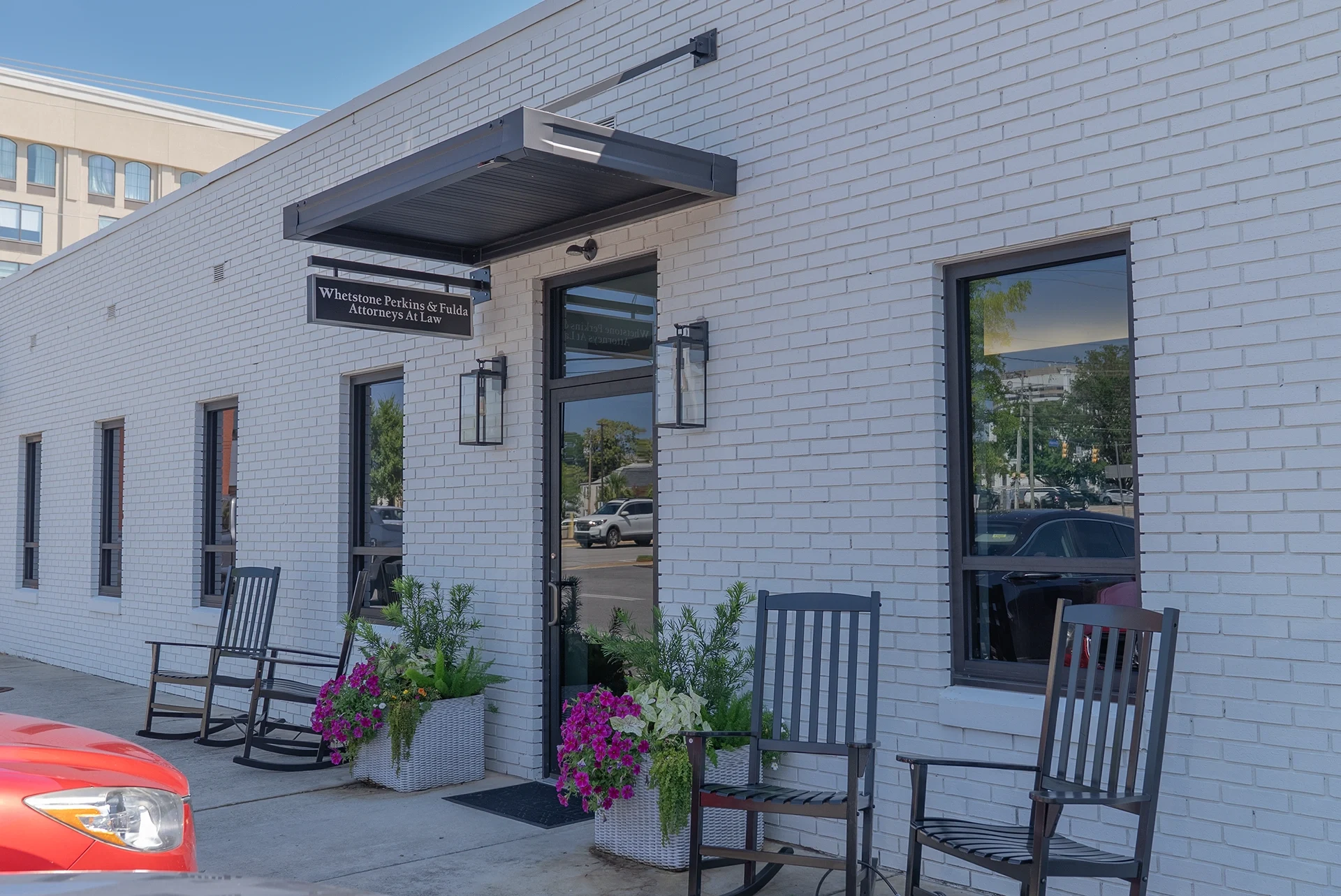 Exterior of a whetstone perkins & fulda attorneys law office with black rocking chairs and flower planters near the entrance on a sunny day