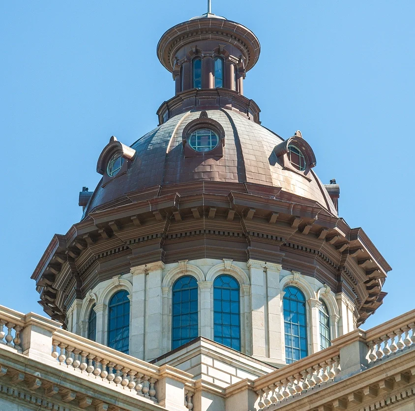 Close-up of a historic building's dome with round windows and ornate stone balustrades against a clear blue sky