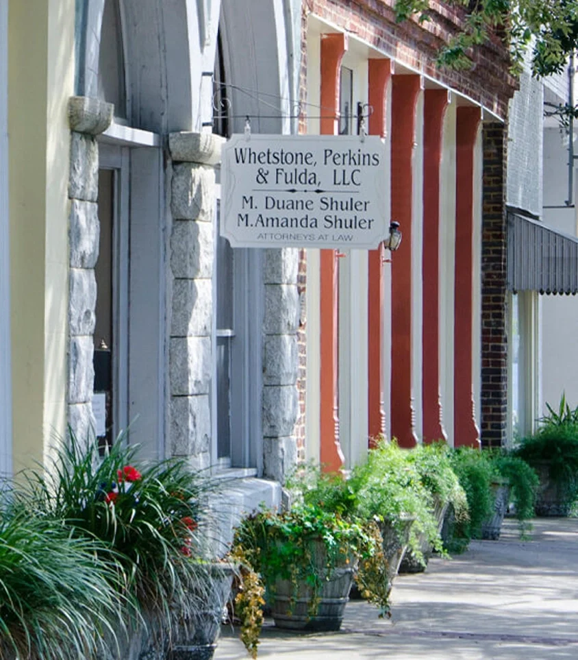Sign for Whetstone, Perkins & Fulda law firm hanging outside a brick building with potted plants lining the sidewalk